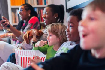 Multi-ethnic family watching movie and eating popcorn on the couch watching a movie with a dog.