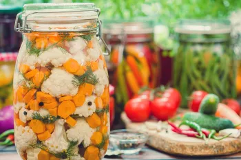 A table full of vegetables on a wooden cutting board and sealed in jars for pickling.