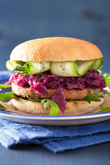 A veggie soy burger with pickled red cabbage cucumber arugula between two buns.